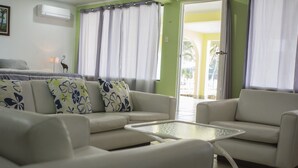 Ein Wohnzimmer mit einer Sofagarnitur, einem Glastisch und Blick ins Freie.