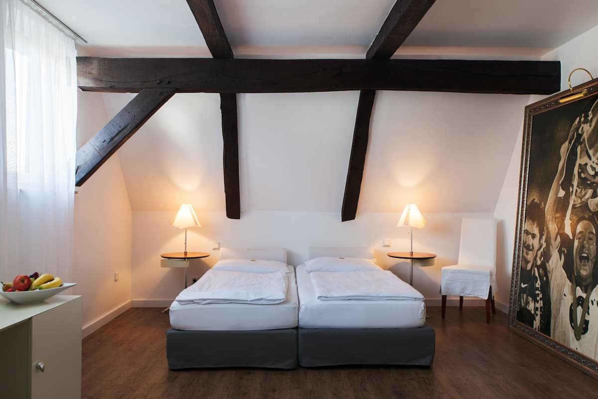 A room with two beds, a chair, a table with fruit, and a painting.