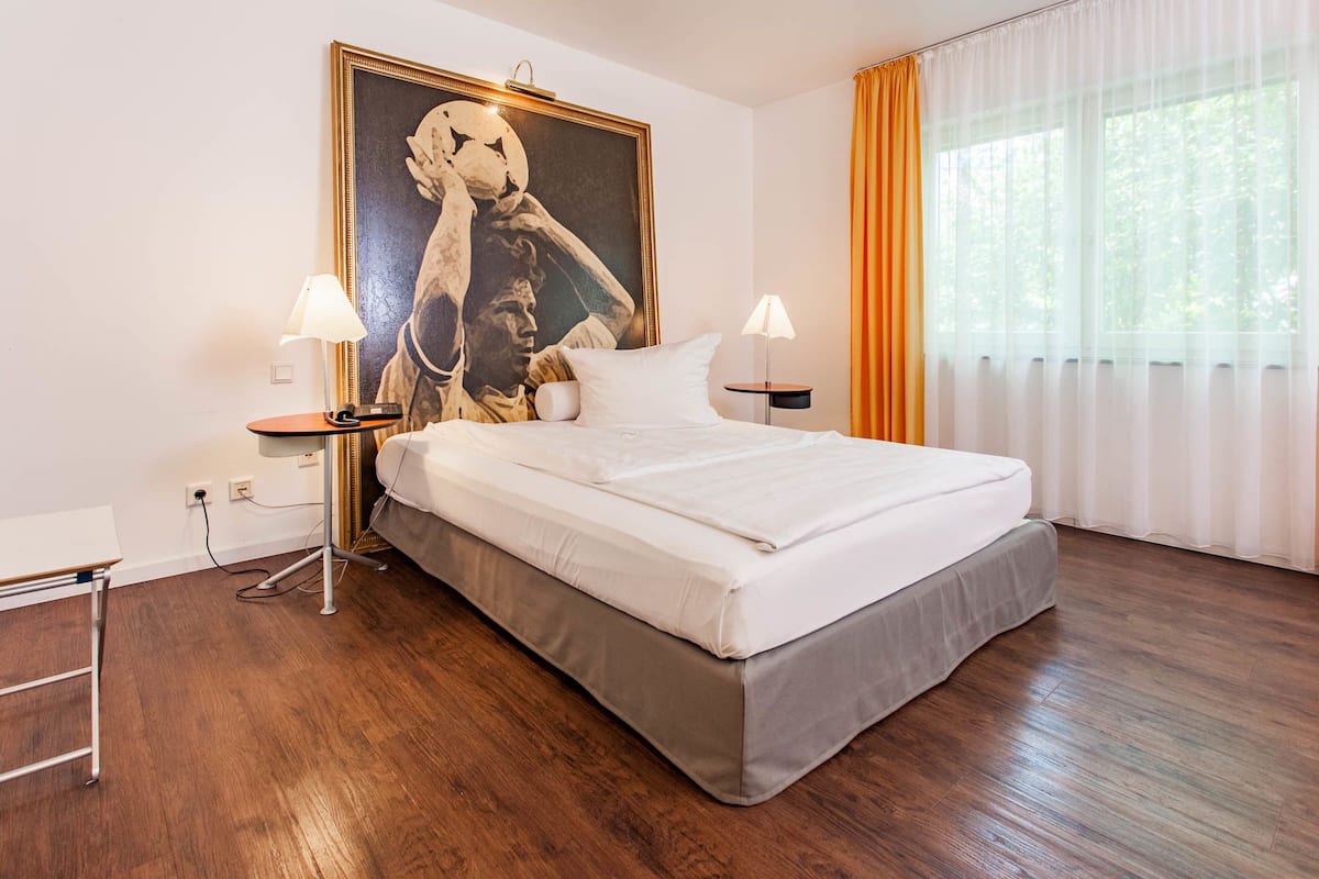 A hotel room with a large bed, two bedside tables, a desk, and a large painting on the wall.