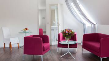 A modern living room with two red armchairs, a glass coffee table, and a small white table with fruit.