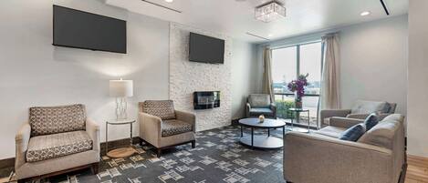 Una habitación de hotel moderna con un televisor de pantalla plana grande montado en la pared, una zona de estar confortable con dos sofás y una silla, una mesita de centro redonda y una alfombra estampada.