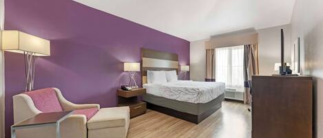 A hotel room with a bed, a desk, a chair, a nightstand, a lamp, and a wardrobe.