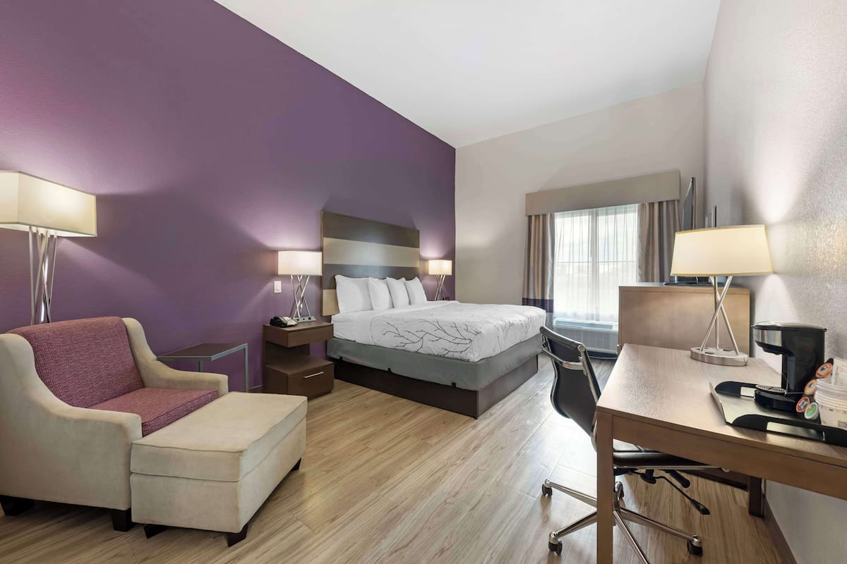 A hotel room with a bed, a desk, a chair, and a sofa.