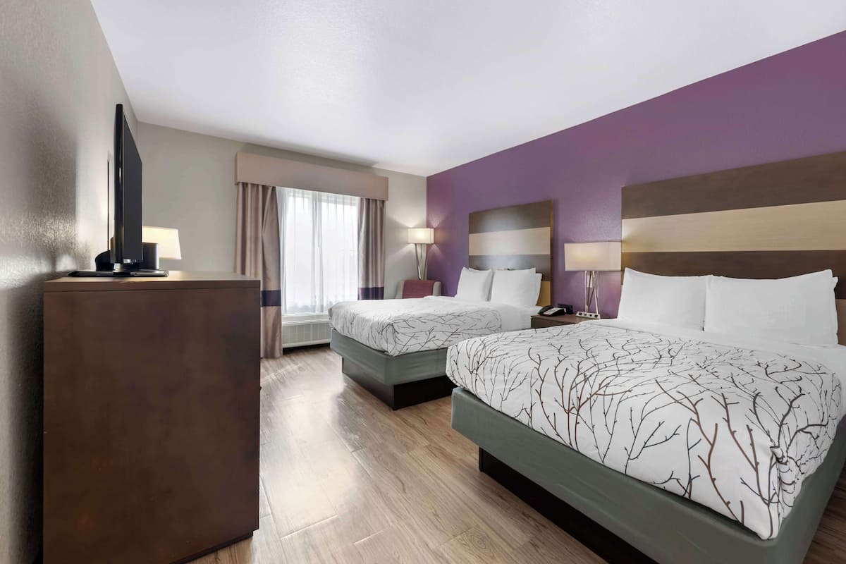 A hotel room with two beds, a TV, a desk, and a window with curtains.
