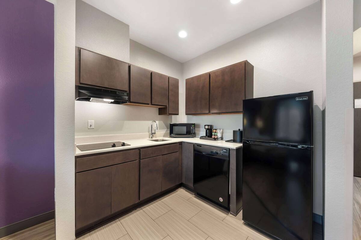 A modern kitchen with dark wooden cabinets, a black refrigerator, a microwave, and a dishwasher.