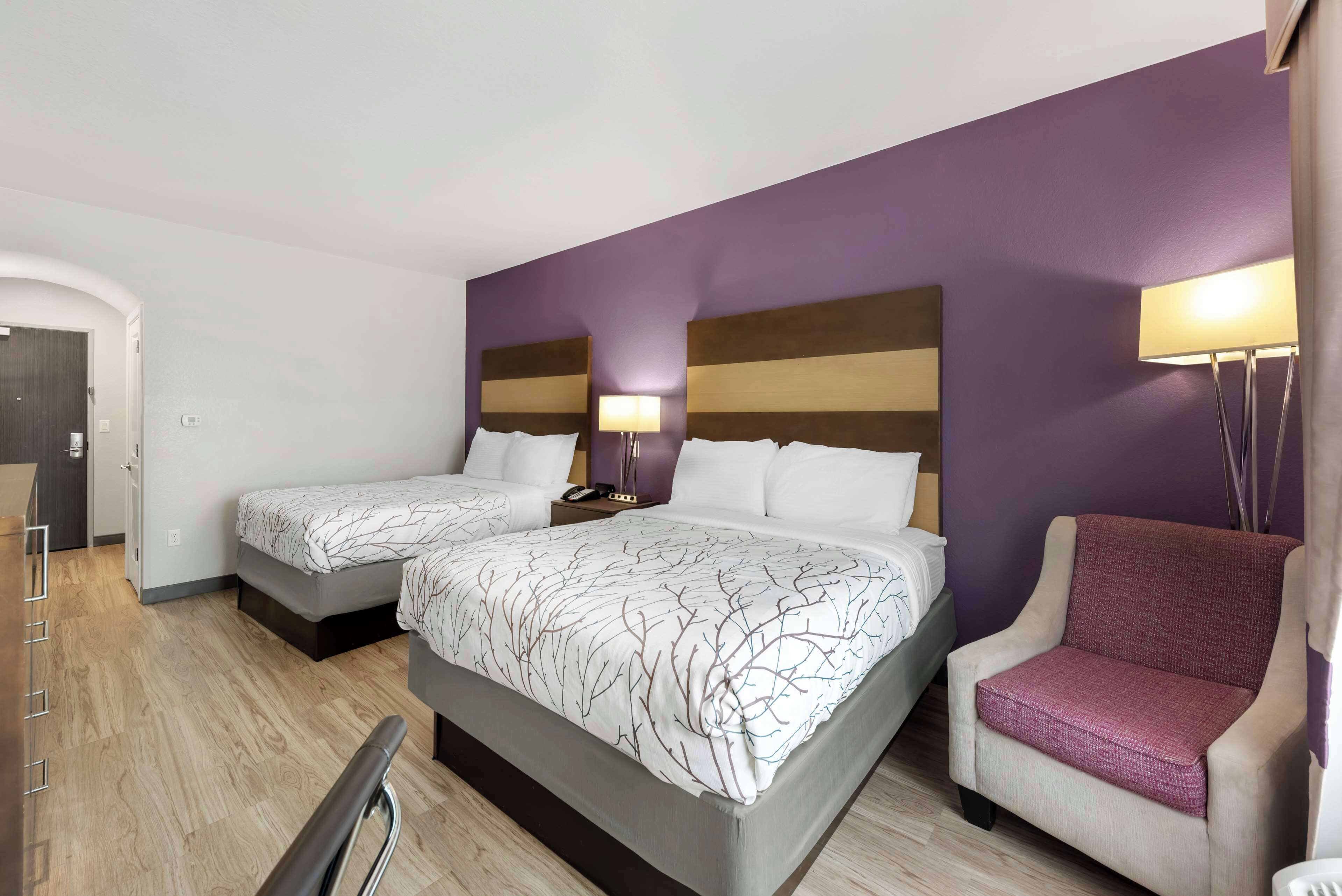 A hotel room with two beds, a chair, and a desk.