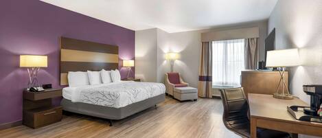 A modern hotel room with a large bed, a desk, a chair, and a TV.