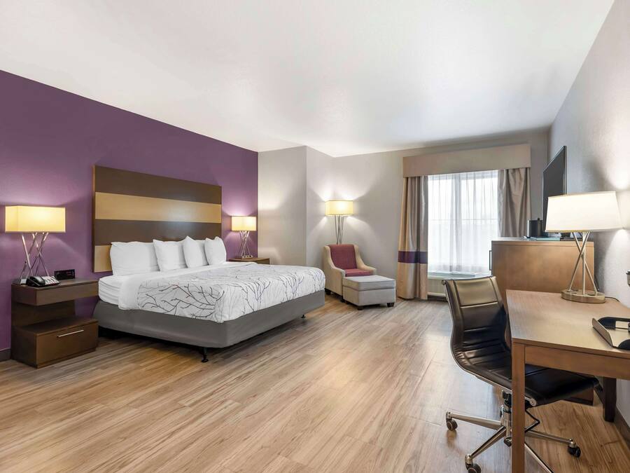 A modern hotel room with a large bed, a desk, a chair, and a TV.