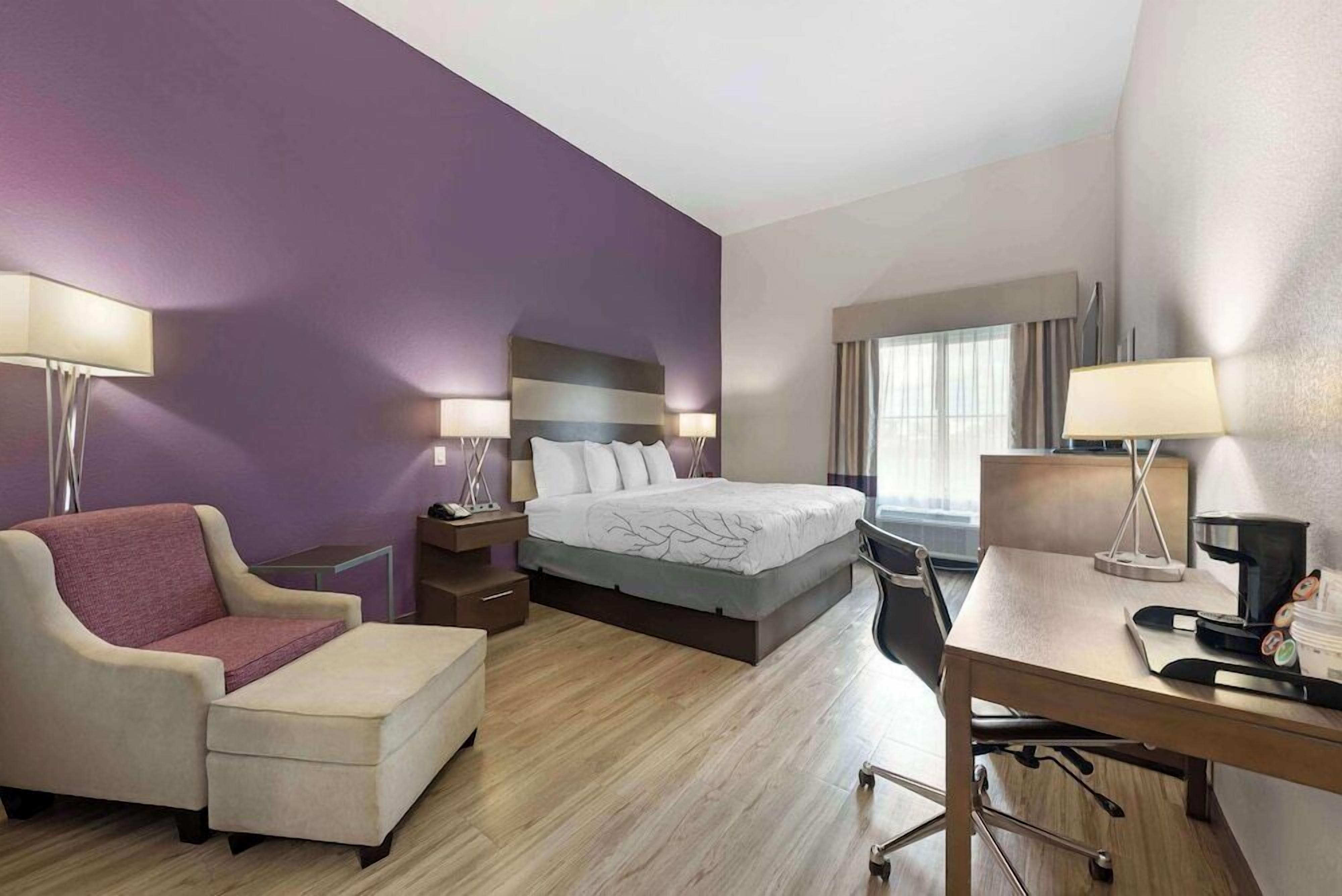 A hotel room with a bed, a desk, a chair, a sofa, and two lamps.