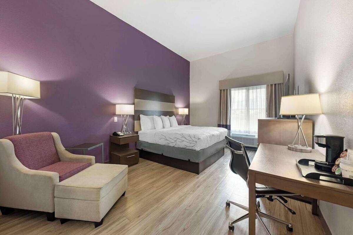 Una habitación de hotel con cama, escritorio, silla, sofá y dos lámparas.