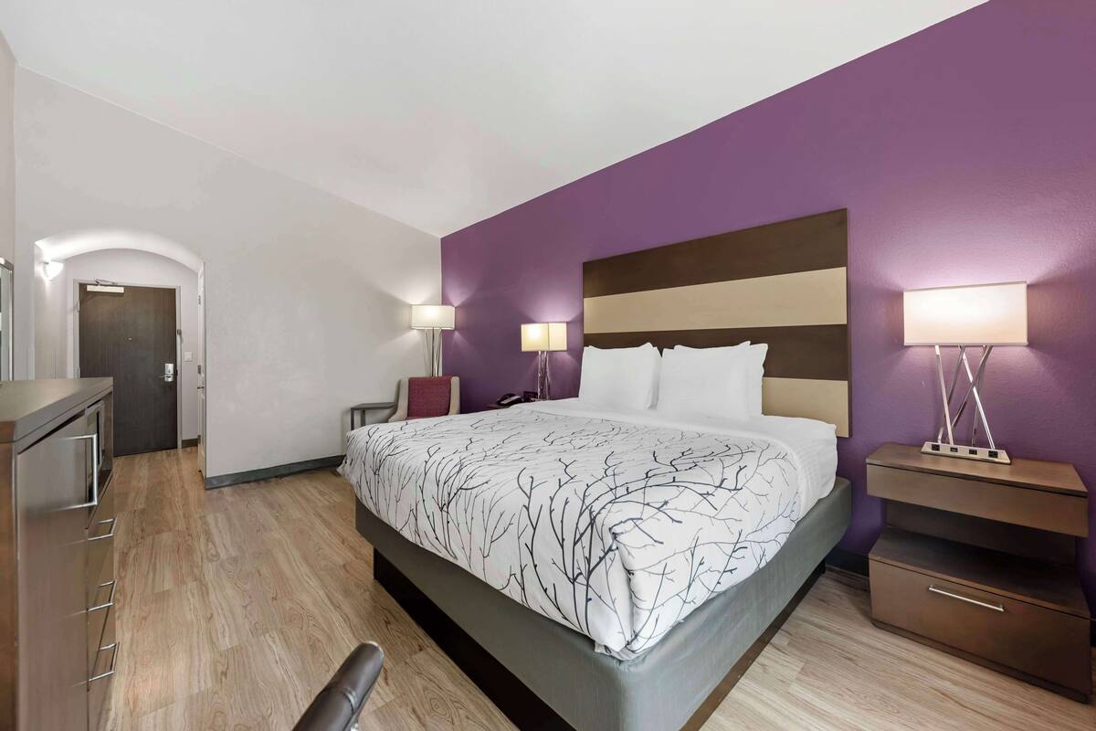 A modern hotel room with a large bed, bedside lamps, a desk, and a wardrobe.