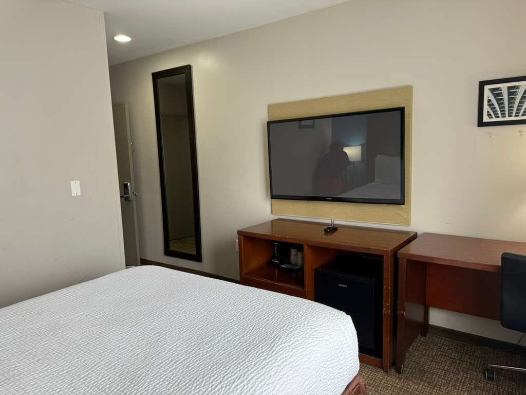 A hotel room with a bed, a desk, a television, and a mirror.