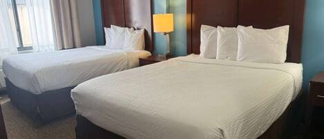 A hotel room with two beds, a nightstand with a lamp, and a view of the outdoors.