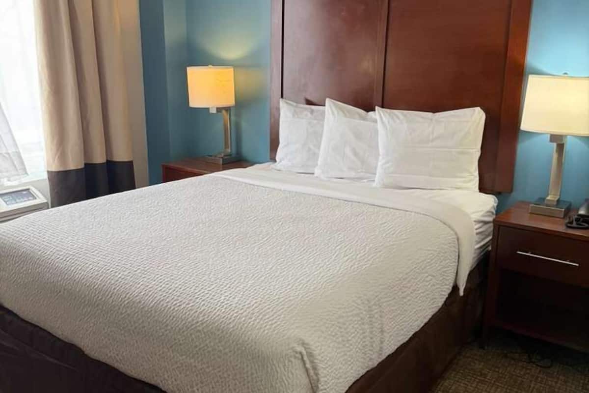 Une chambre d’hôtel avec un grand lit, deux tables de chevet et une fenêtre avec des rideaux.