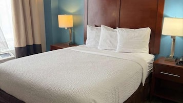A hotel room with a large bed, two bedside tables, and a window with curtains.