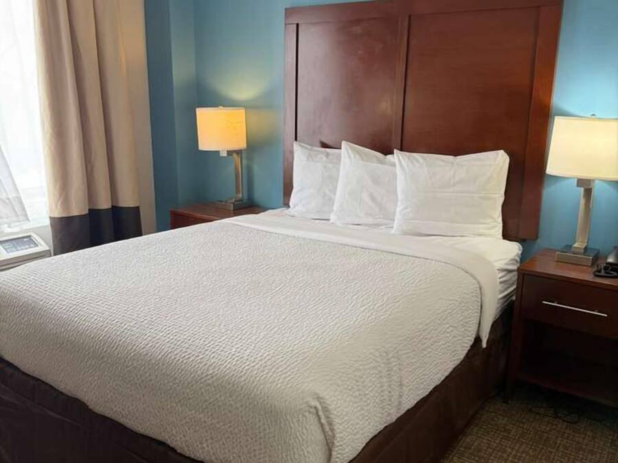 A hotel room with a large bed, two bedside tables, and a window with curtains.