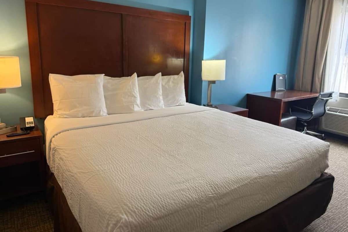 Une chambre d’hôtel avec un grand lit, une tête de lit en bois, un bureau et une chaise.