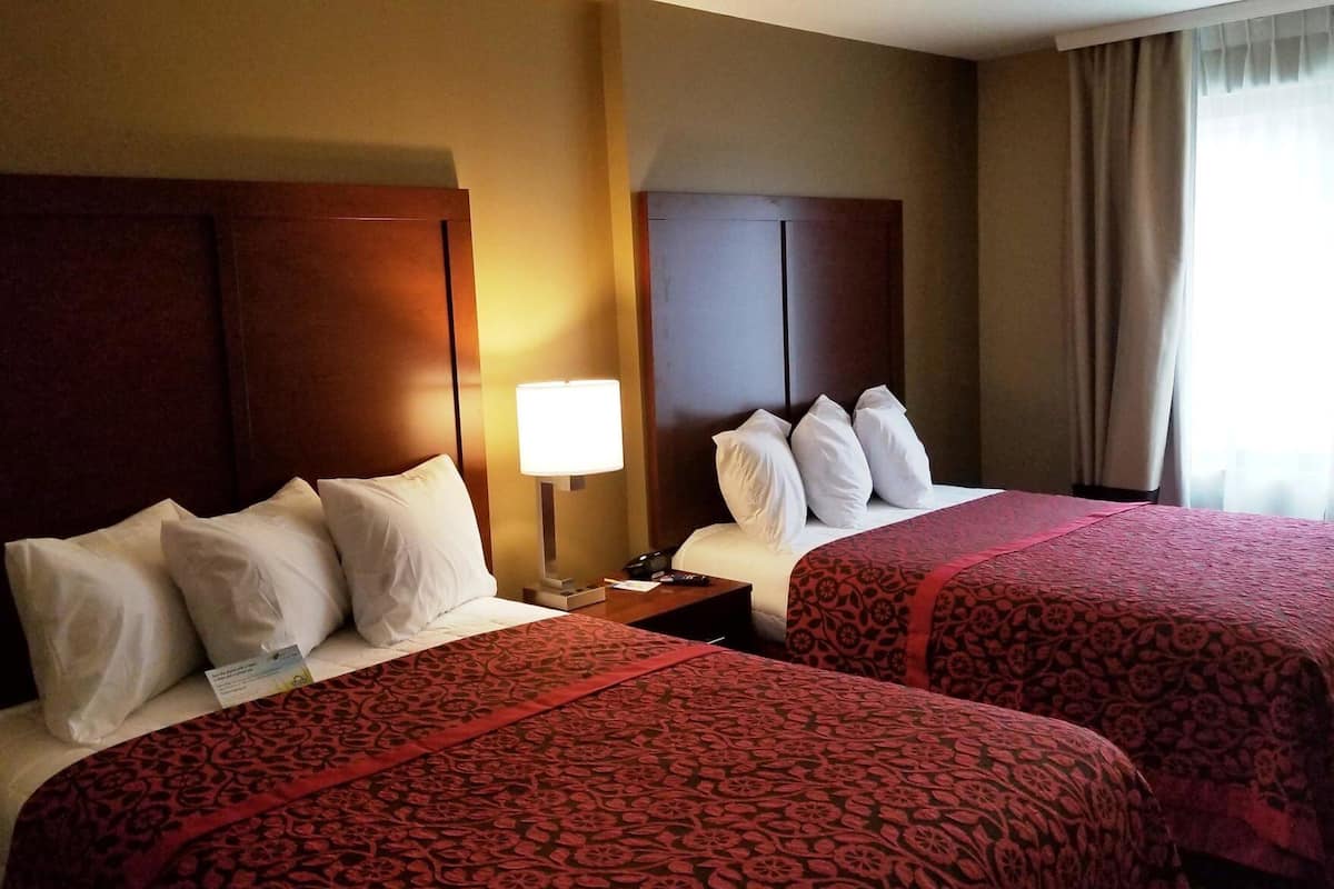 Une chambre d’hôtel avec deux lits, une table de chevet, une lampe et une fenêtre avec des rideaux.