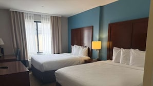 Een hotelkamer met twee bedden, een bureau, een stoel en een raam met gordijnen.