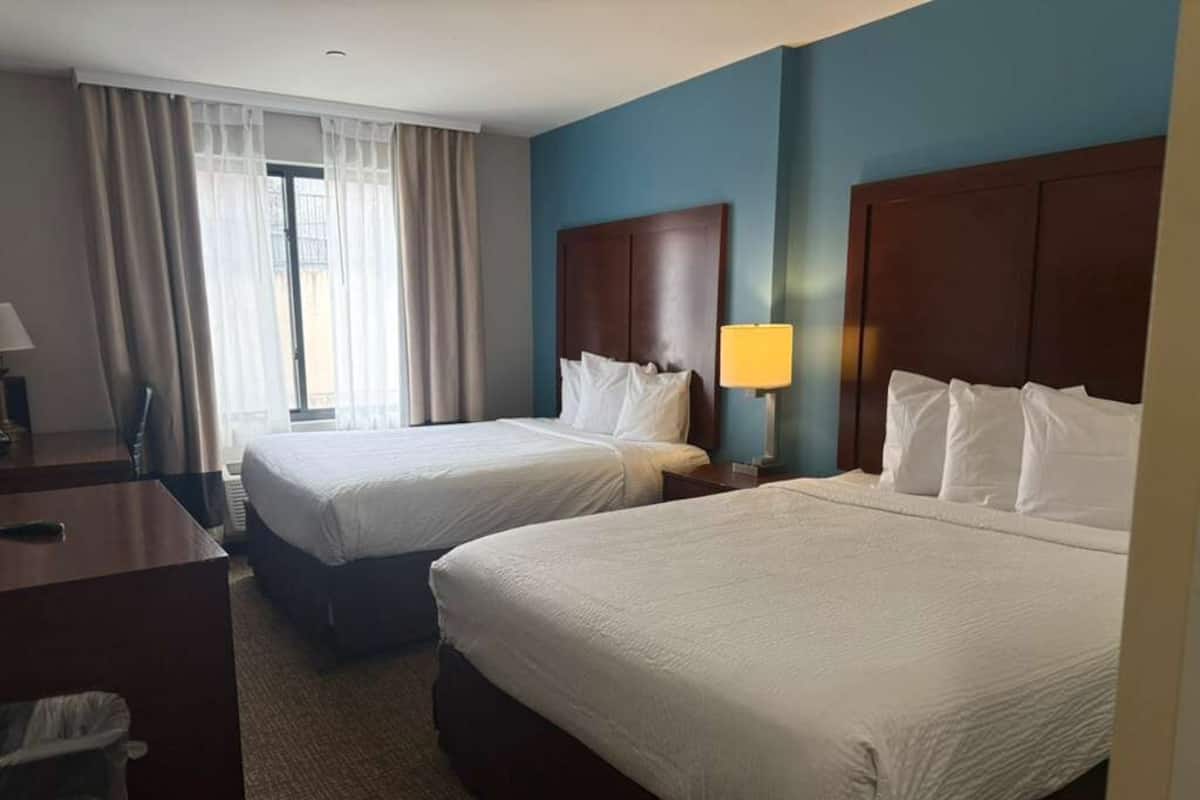 Une chambre d’hôtel avec deux lits, un bureau, une chaise et une fenêtre avec des rideaux.