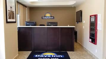 A reception desk with a Days Inn logo, a flat-screen TV, a fire alarm, and a patterned carpet.