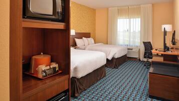 A hotel room with two beds, a microwave, a coffee maker, a desk with a computer, and a window with curtains.