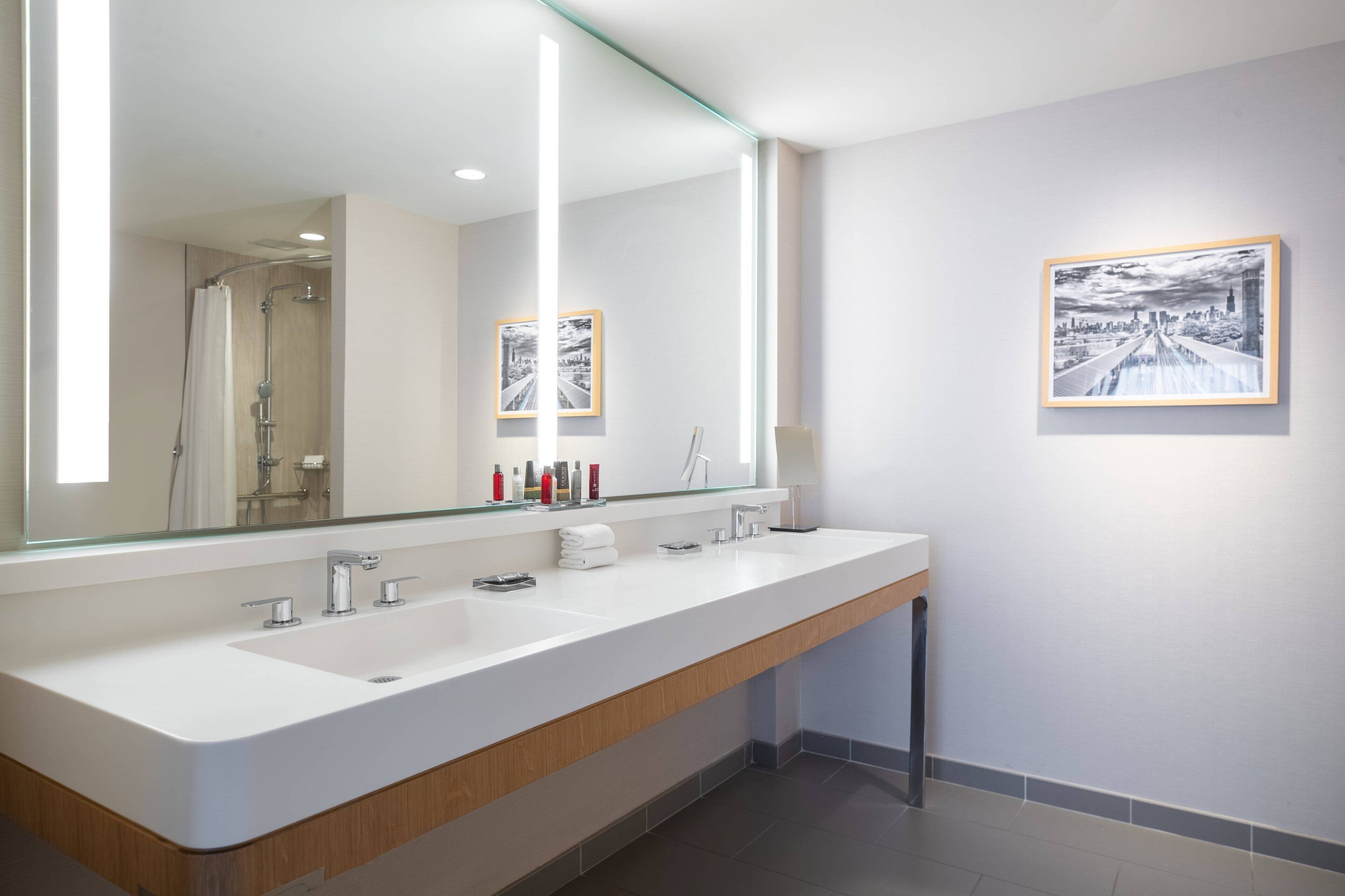 Un baño moderno con un espejo grande, dos lavamanos y cuadros enmarcados en la pared.
