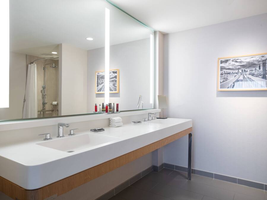 Un baño moderno con un espejo grande, dos lavamanos y cuadros enmarcados en la pared.