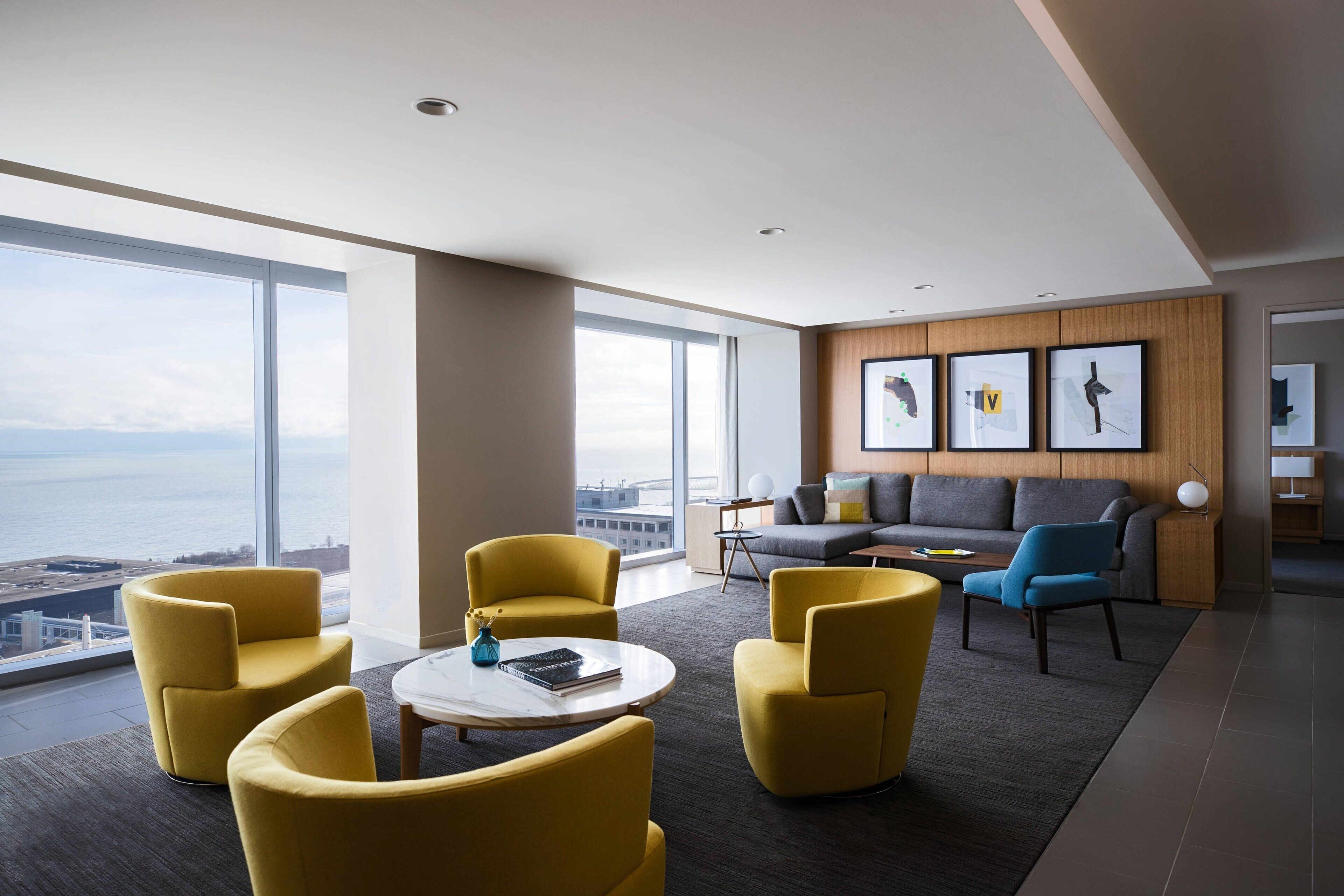 A modern living room with large windows, a gray sofa, yellow armchairs, and a coffee table.