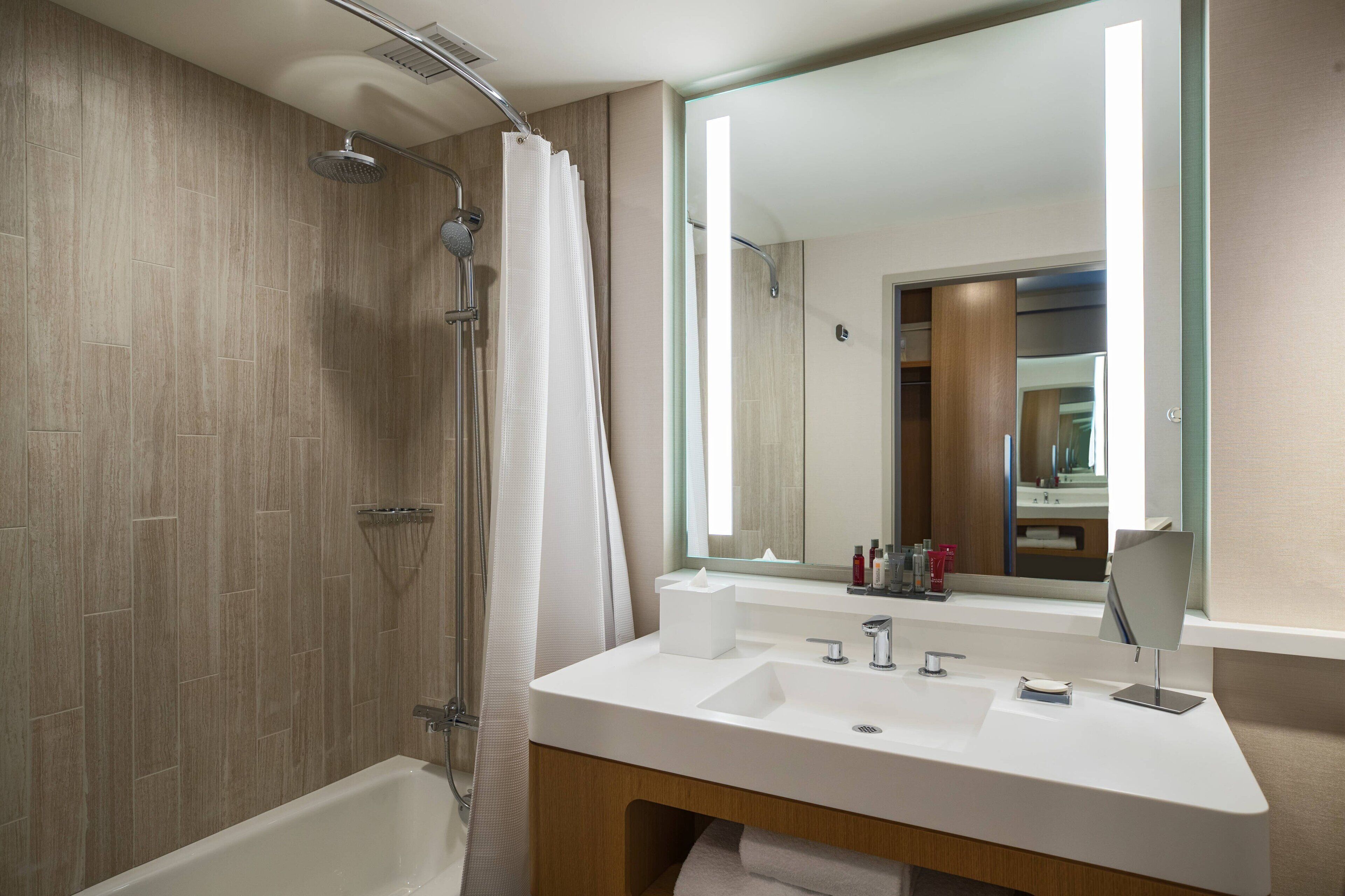 A modern bathroom with a shower, a large mirror, and a vanity with a sink and towel rack.