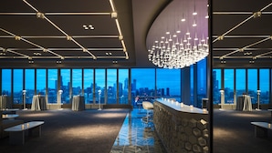 A modern hotel lobby with a city view, a bar area, and seating arrangements.