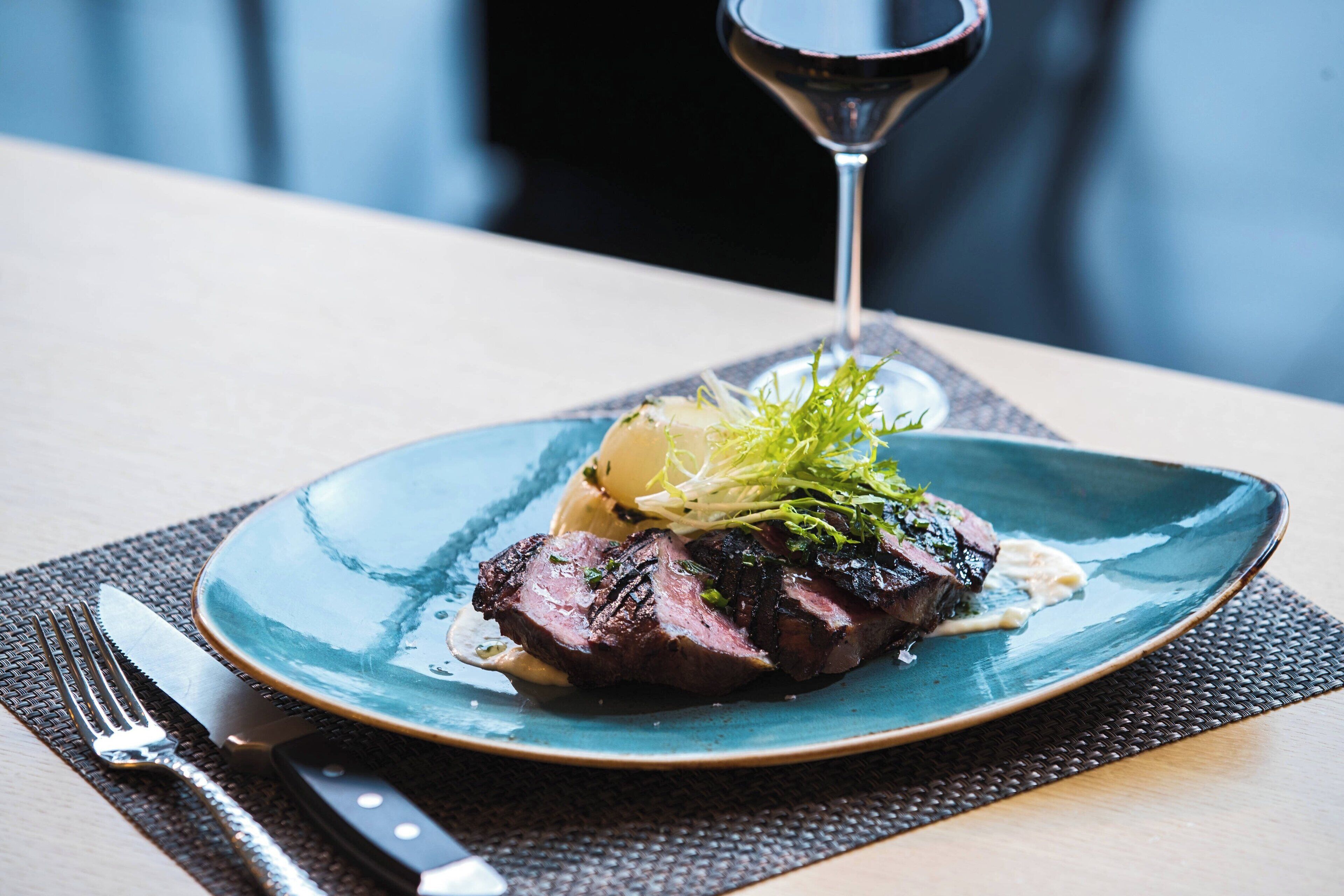 A plate of steak with a garnish and sauce, accompanied by a wine glass.