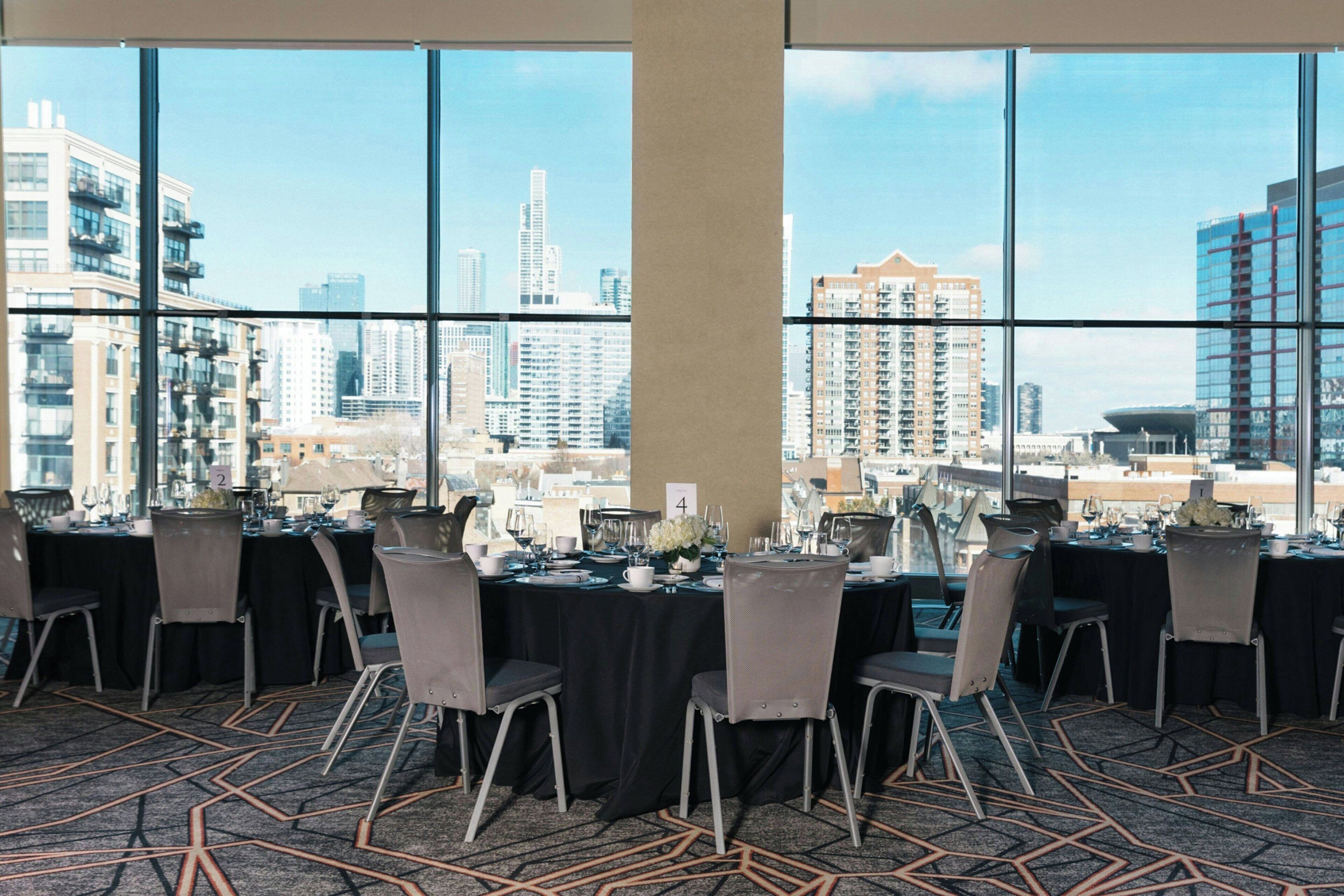 Un salón de conferencias con mesas dispuestas para una reunión, amplias ventanas con vistas a la ciudad.