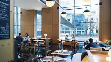 Ein modernes Restaurant mit hohen Decken, großen Fenstern und einer Mischung aus Sitzbereichen, darunter Tische und Sofas.