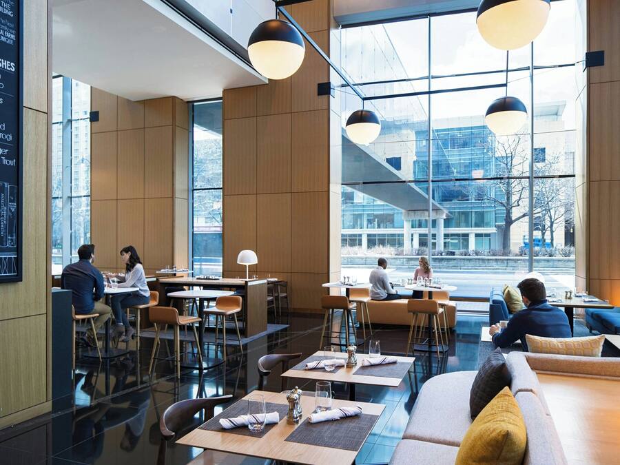 Ein modernes Restaurant mit hohen Decken, großen Fenstern und einer Mischung aus Sitzbereichen, darunter Tische und Sofas.
