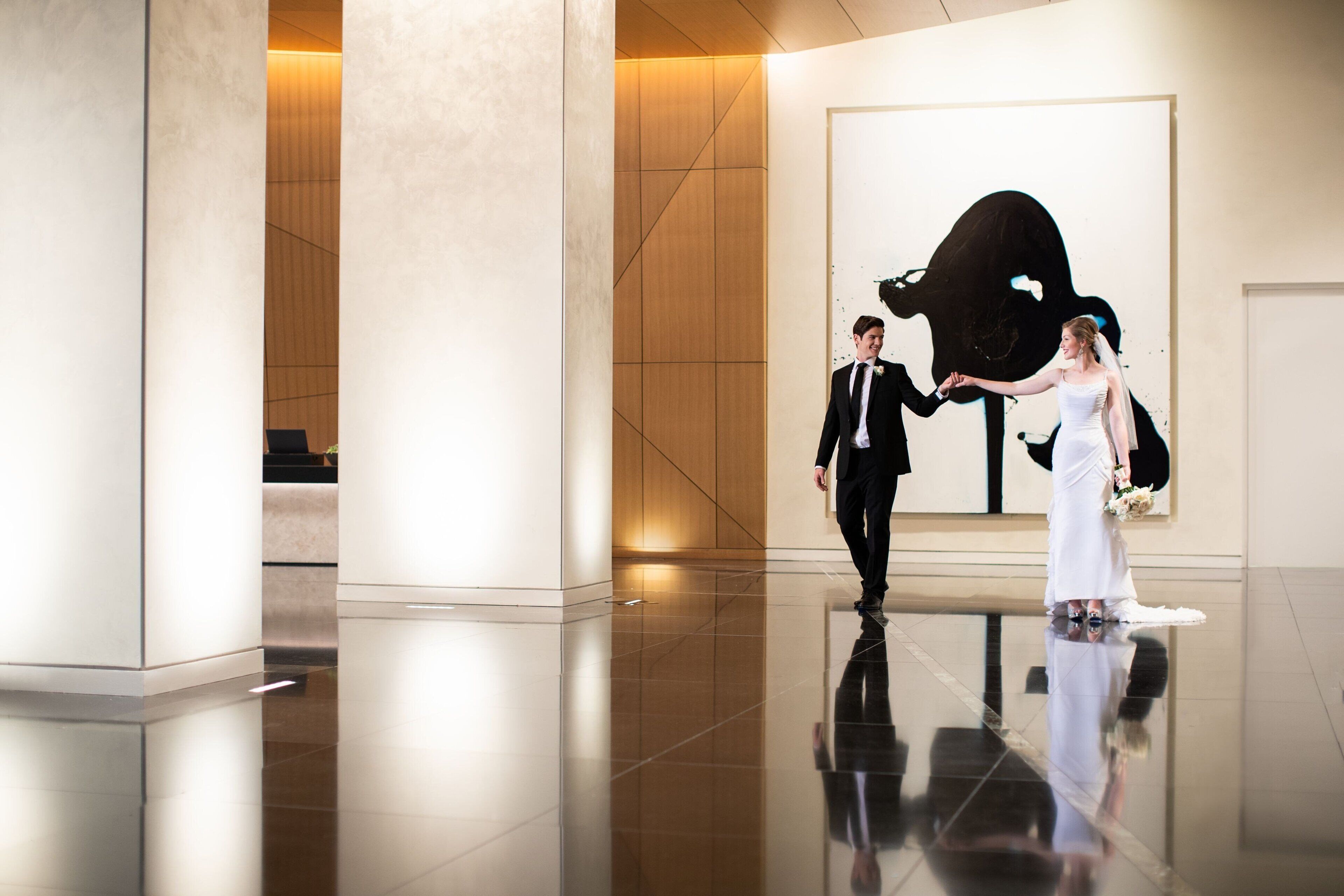 A modern hotel lobby with a polished floor, large columns, and a large abstract artwork on the wall.