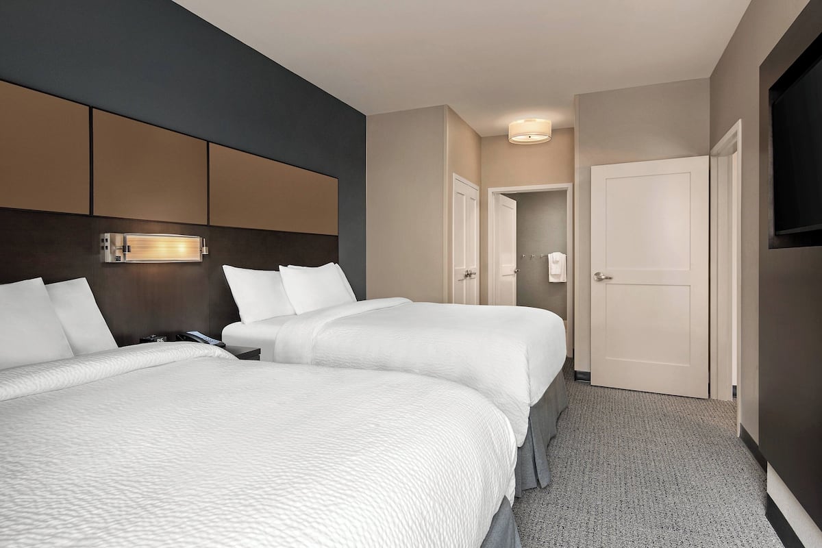 A hotel room with two beds, a headboard with built-in lighting, a walk-in closet, and a television mounted on the wall.