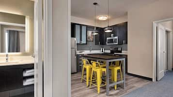 A modern kitchen with dark cabinets, a central island with yellow chairs, and pendant lighting.