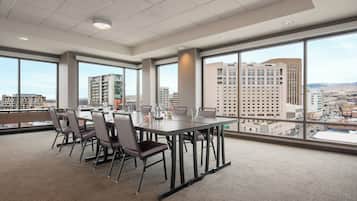A conference room with a large table and chairs, large windows with a city view, and a carpeted floor.