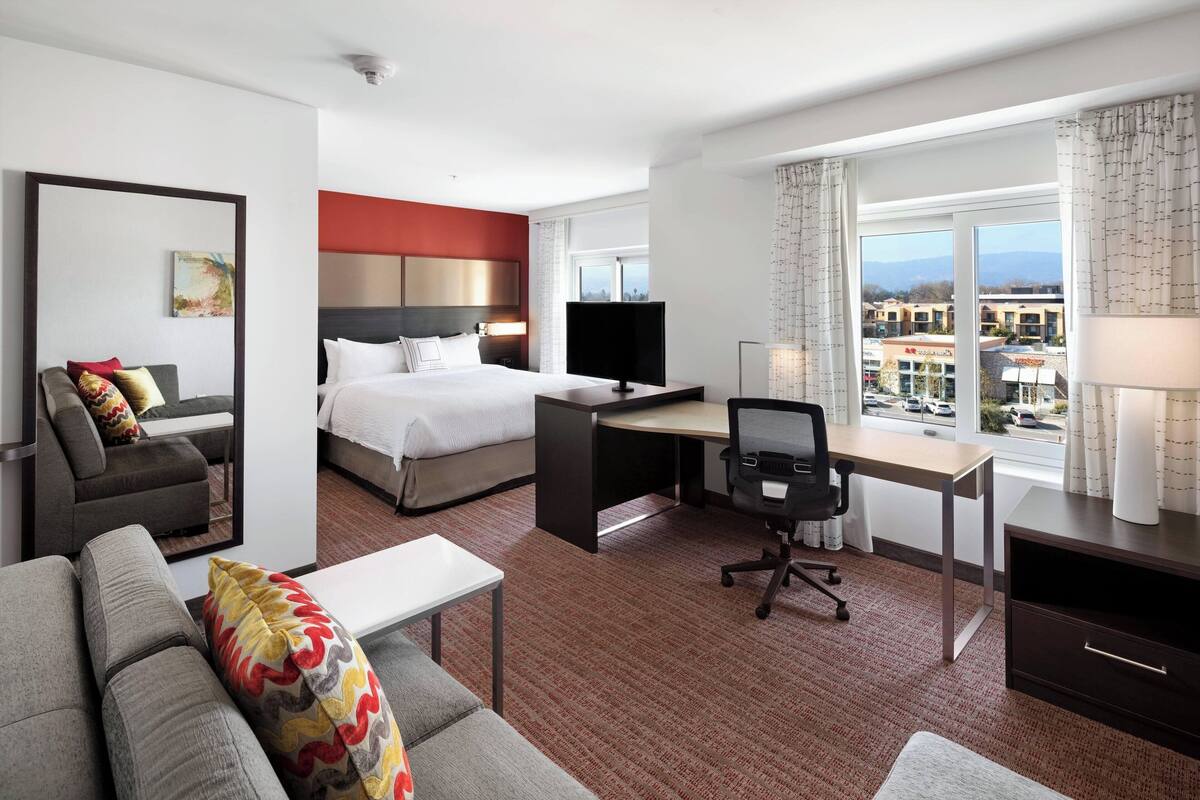 A hotel room with a bed, a desk, a sofa, and a view of buildings.