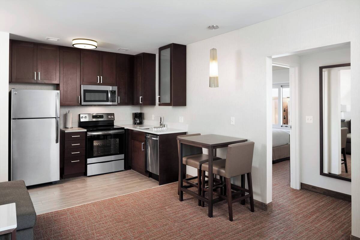 A modern kitchen with dark cabinets, stainless steel appliances, and a small dining area with two chairs.