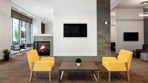 Un vestíbulo moderno con chimenea, dos sillones amarillos, un televisor de pantalla plana montado en la pared y un amplio ventanal que proporciona luz natural.