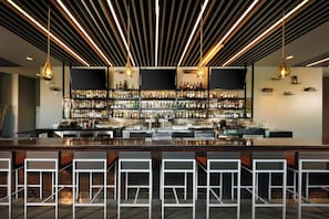 A bar area with a long counter, multiple shelves of bottles, and hanging light fixtures.