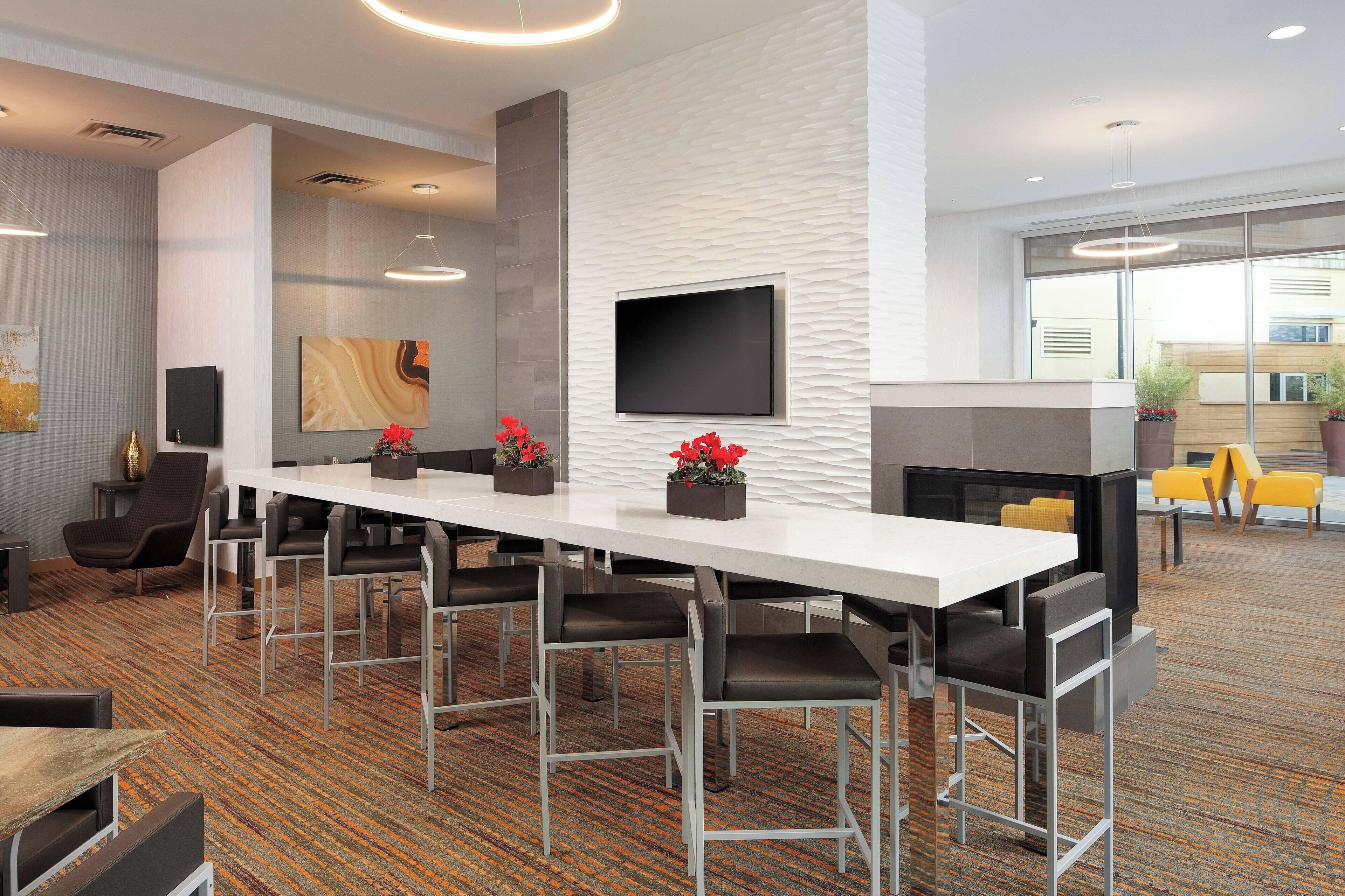 A modern conference room with a long table, multiple chairs, a flat-screen TV, and a fireplace.