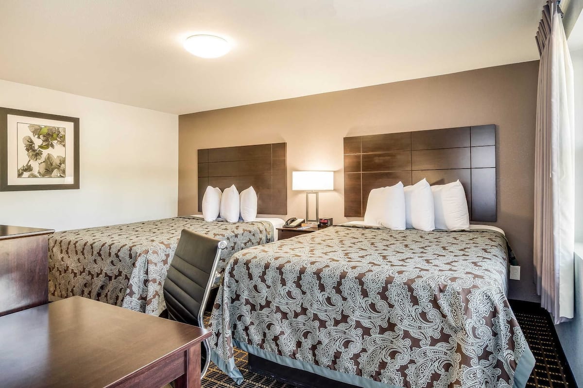 A hotel room with two beds, a desk, and a chair.