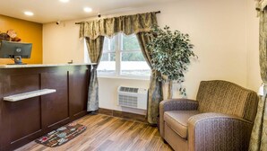 A cozy room with a wooden desk, a chair, a large window with curtains, and a potted plant. - Rodeway Inn Middleboro - Plymouth (Middleborough)