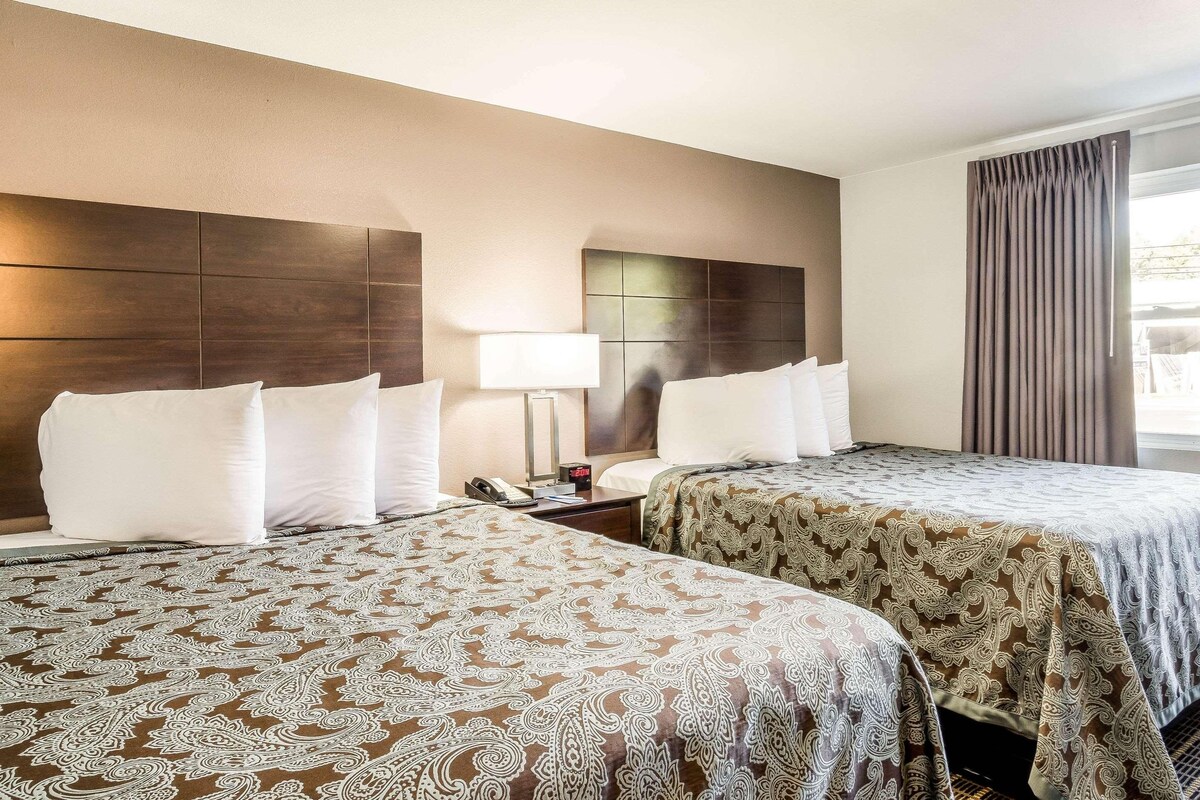 A hotel room with two beds, a nightstand, a lamp, and a clock.