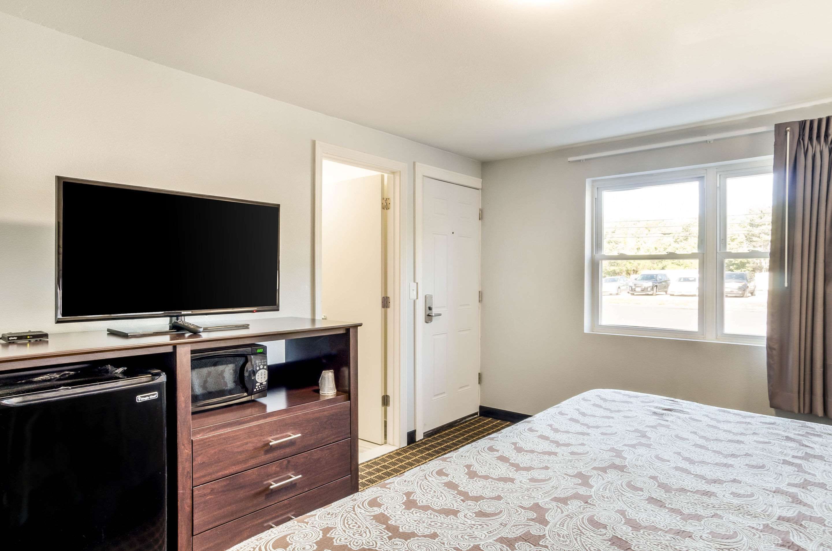 Quarto de hotel com cama, TV, micro-ondas, geladeira e janela com cortinas.