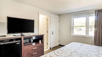 Quarto de hotel com cama, TV, micro-ondas, geladeira e janela com cortinas.
