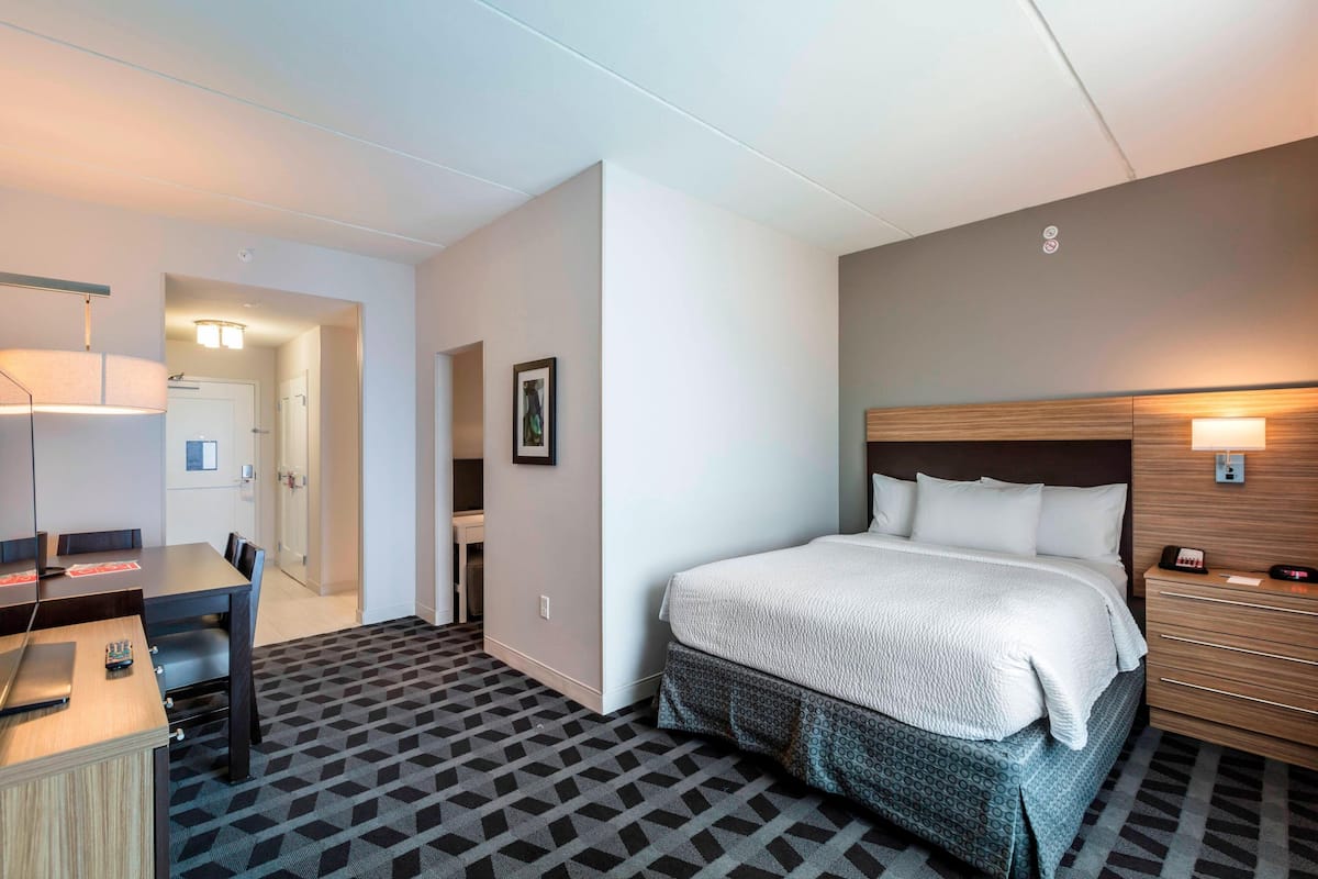 A hotel room with a bed, bedside table, lamp, desk, chair, and patterned carpet.